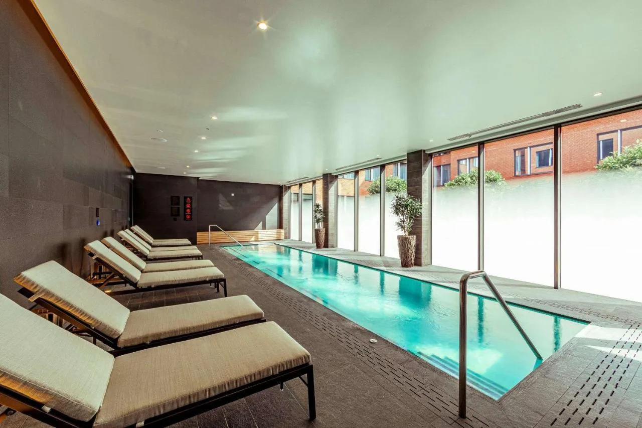 a swimming pool with chaise lounges in a building at The Fellows House Cambridge, Curio Collection By Hilton in Cambridge
