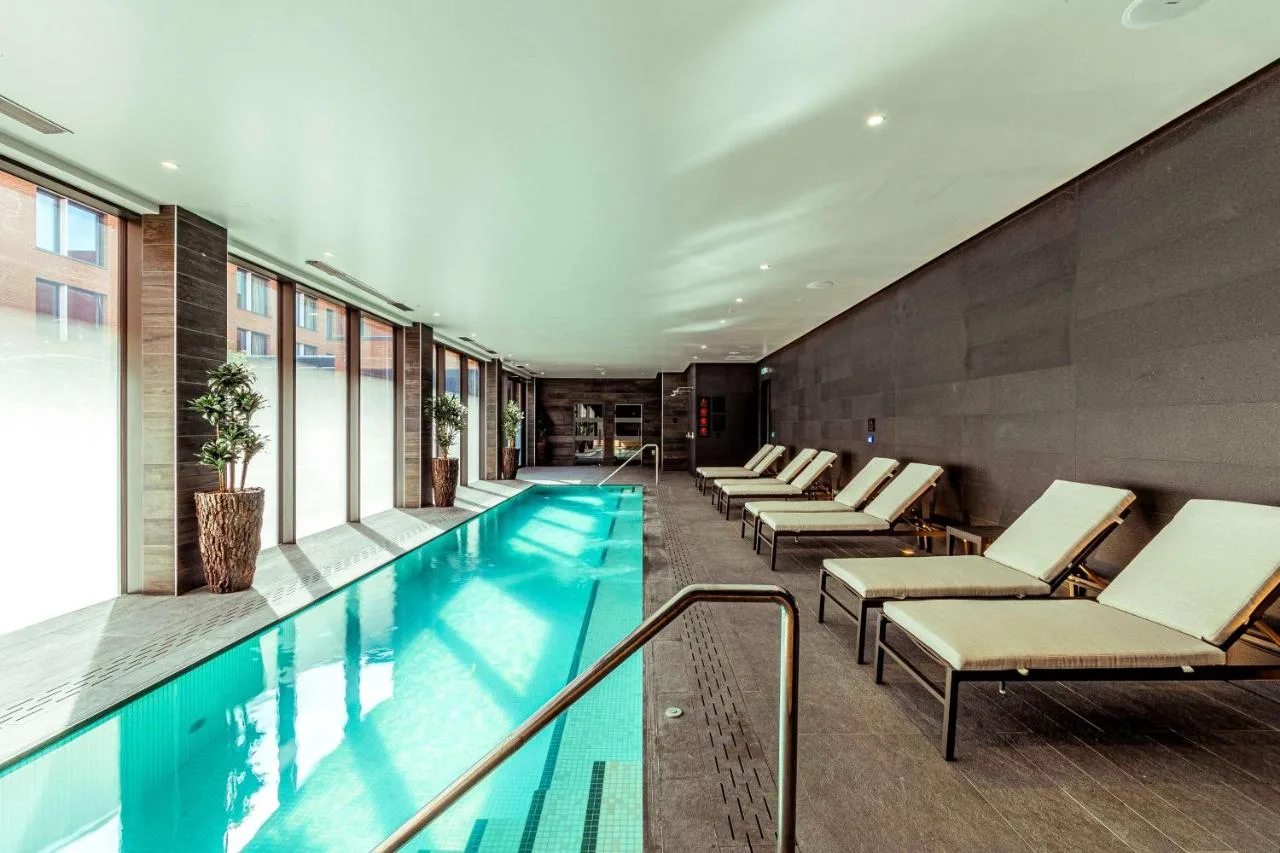 a swimming pool in a building with lounge chairs at The Fellows House Cambridge, Curio Collection By Hilton in Cambridge