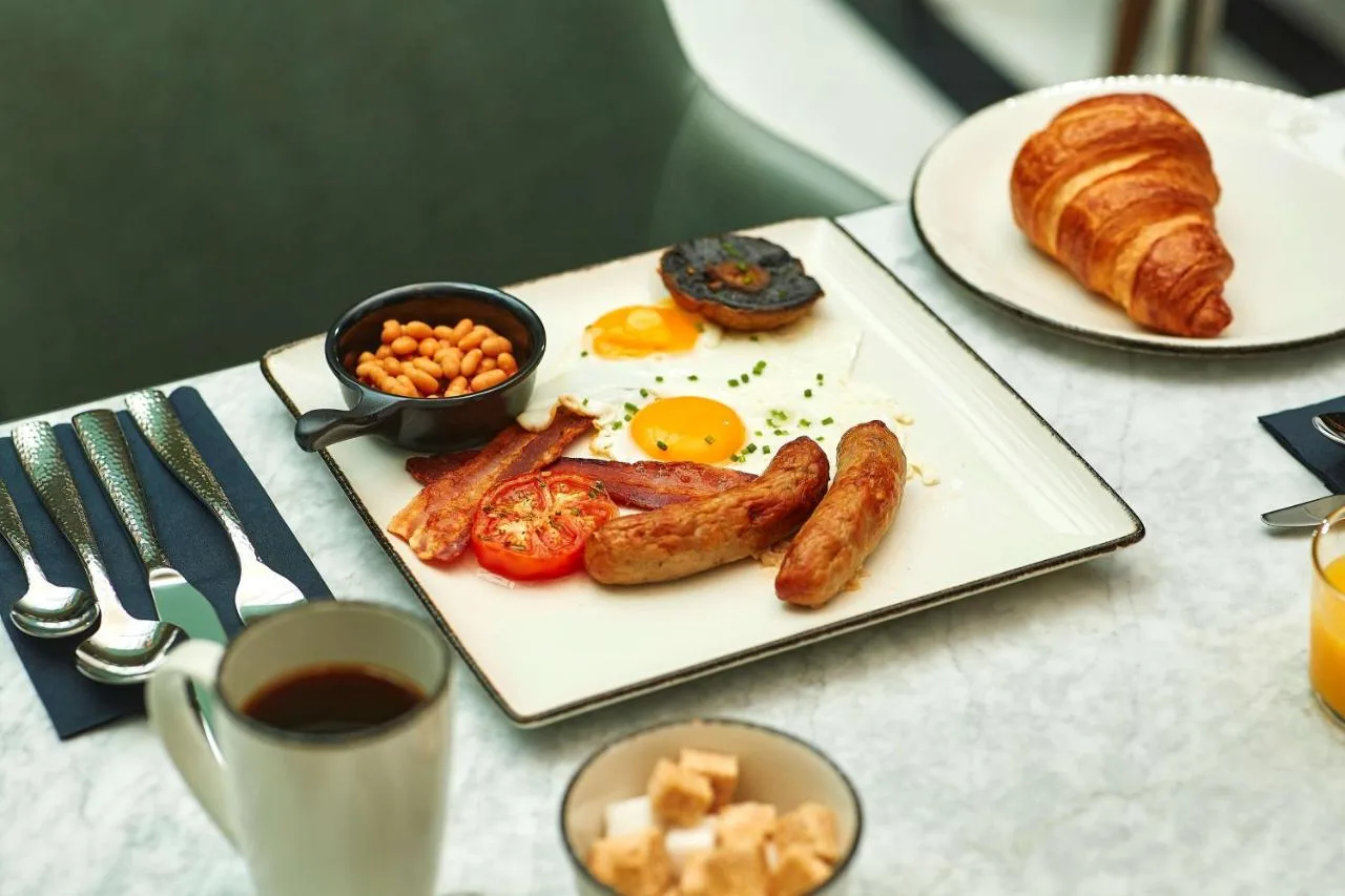a breakfast plate with eggs sausage and beans and croissants at The Fellows House Cambridge, Curio Collection By Hilton in Cambridge
